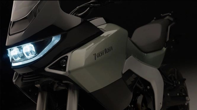 Front three-quarter close-up of a Verona Green Norton Atlas adventure motorcycle showing the illuminated LED headlight and prominent fuel tank branding.