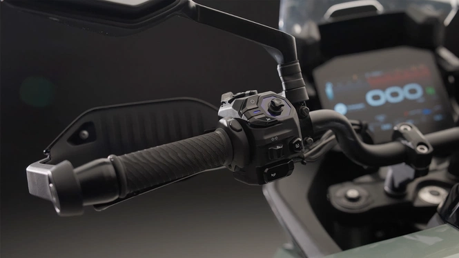 Left handlebar of the Norton Atlas motorcycle featuring complex switchgear, a handguard, and the 8-inch digital TFT touchscreen console blurred in the background.