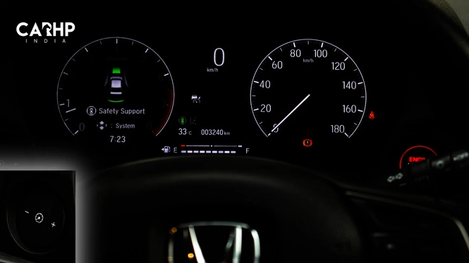 Honda Amaze's Illuminated instrument panel featuring a digital display on the left indicating safety support systems, a traditional analog speedometer on the right, and the top of a Honda steering wheel at the bottom